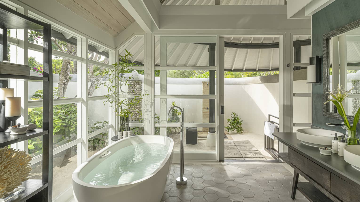 Luxury bathroom with walls of windows and standalone tub, opening to outdoor shower and garden at tropical resort
