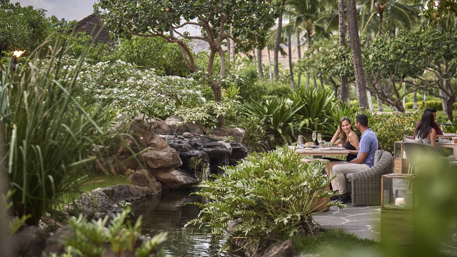 Couple sitting at table surrounded by lush greenery at contemporary outdoor restaurant