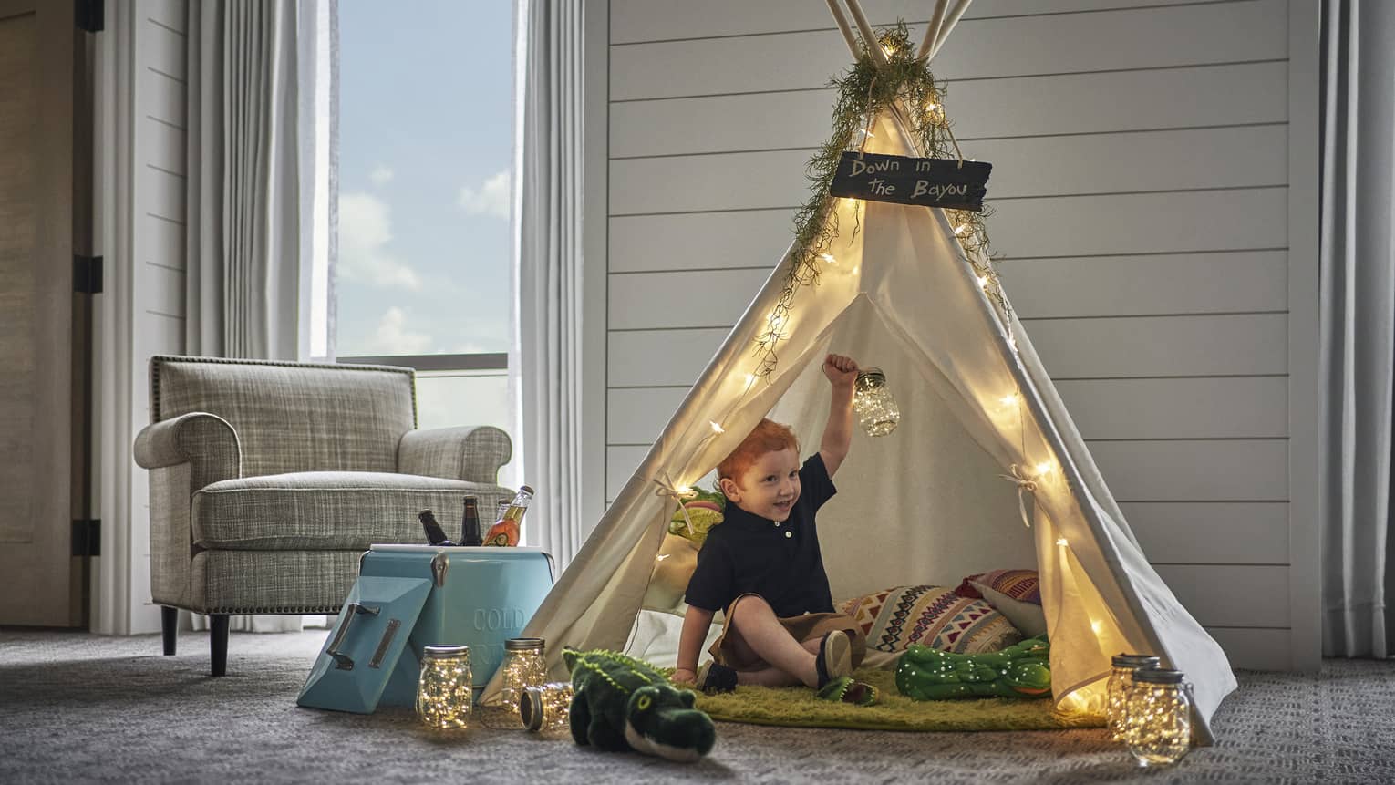 A young boy sitting in a tent with toys in a hotel room.