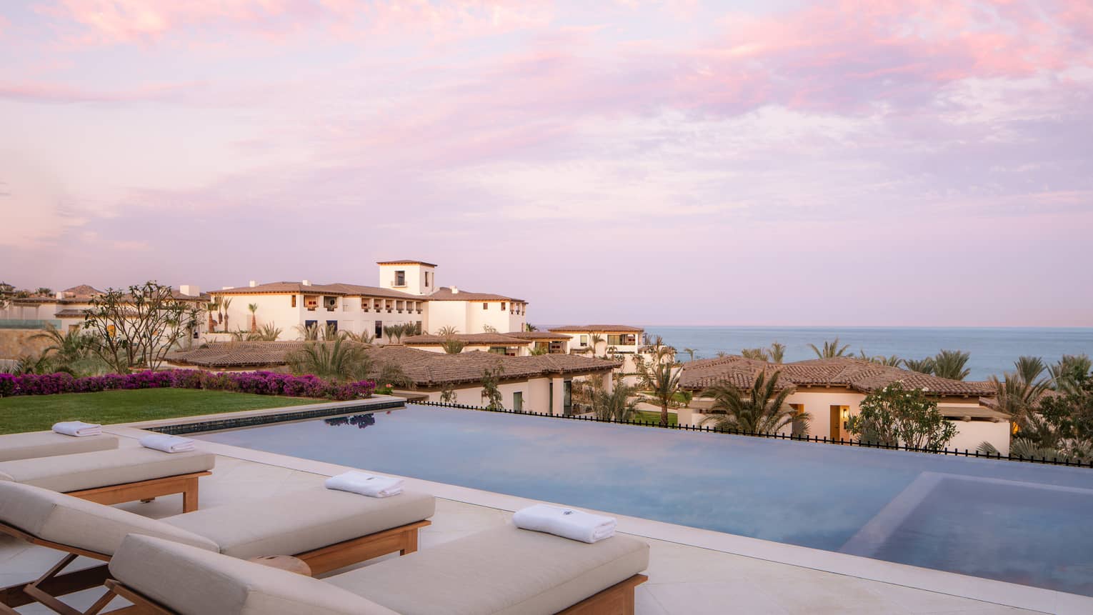 View of a villa terrace with infinity pool, overlooking resort and ocean at sunset