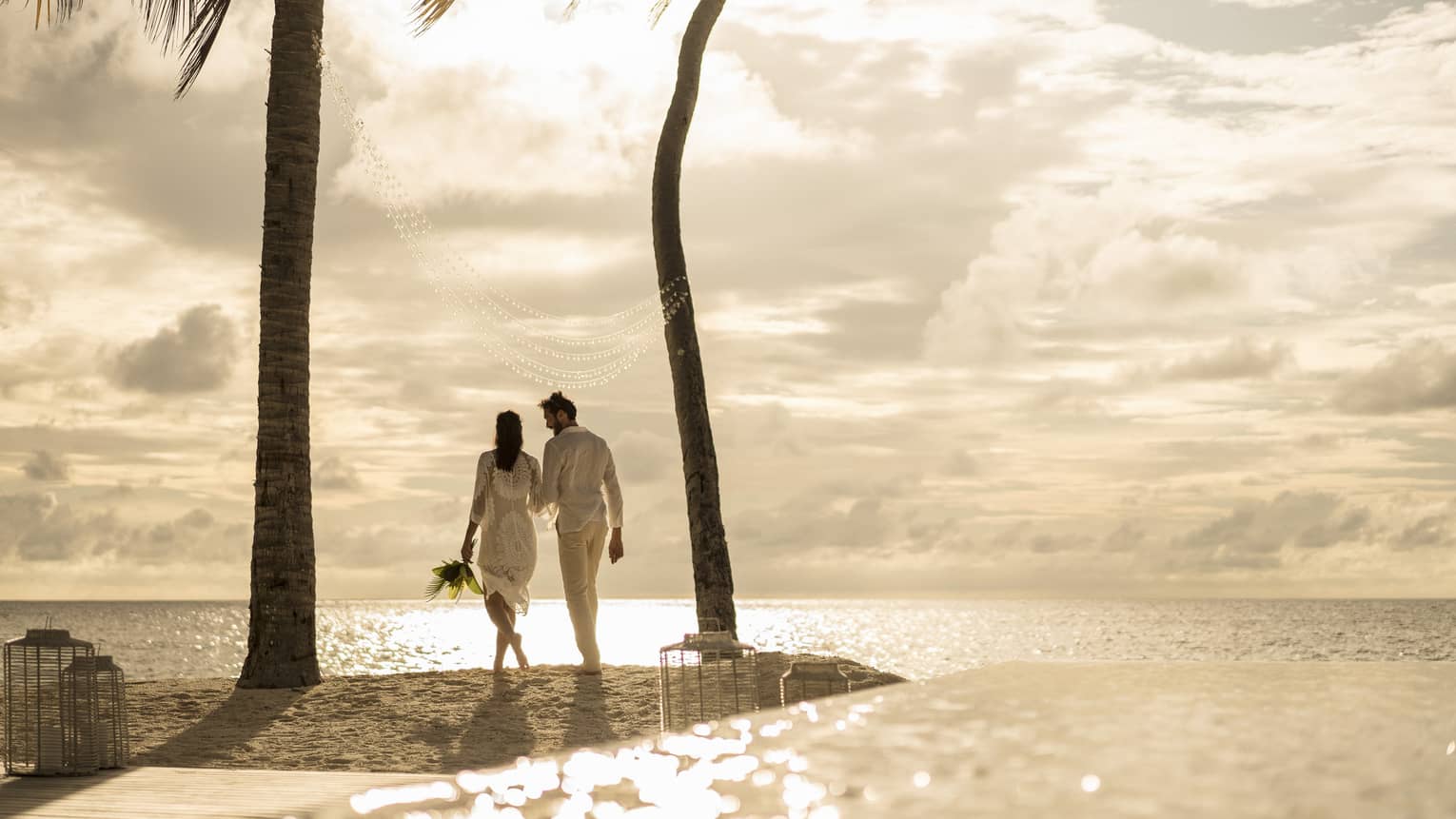 Bride and groom walking towards sunset on white sand beach