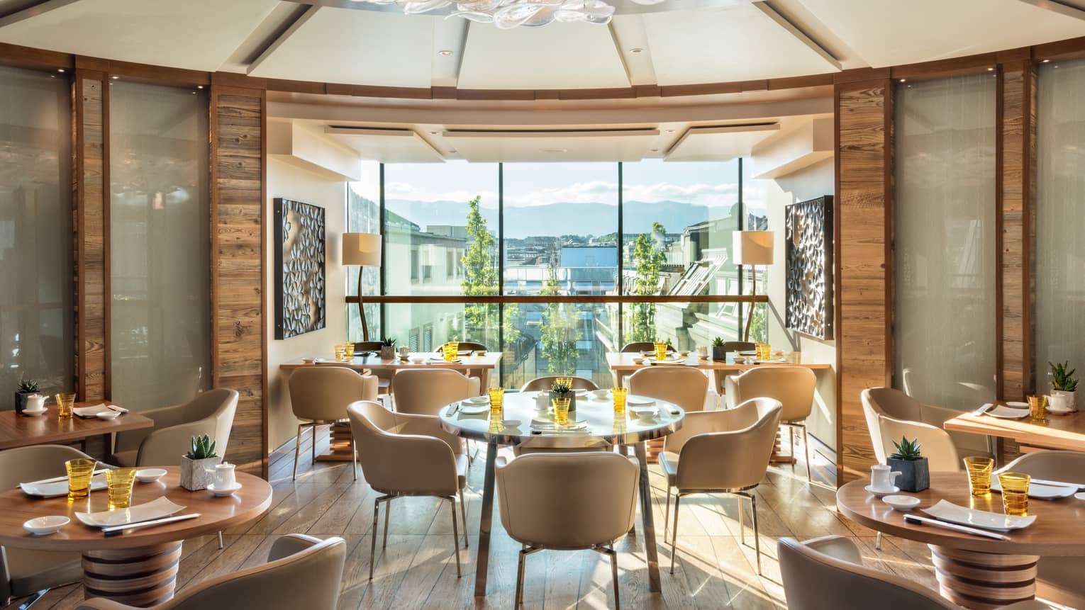 Sunny rotunda dining room with cream-coloured chairs, round wood tables, floor-to-ceiling window