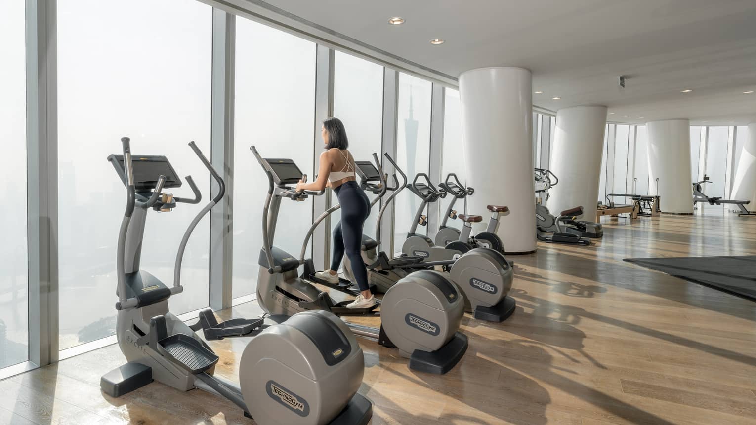 Woman on stairstepper works out in fitness room with floor-to-ceiling windows