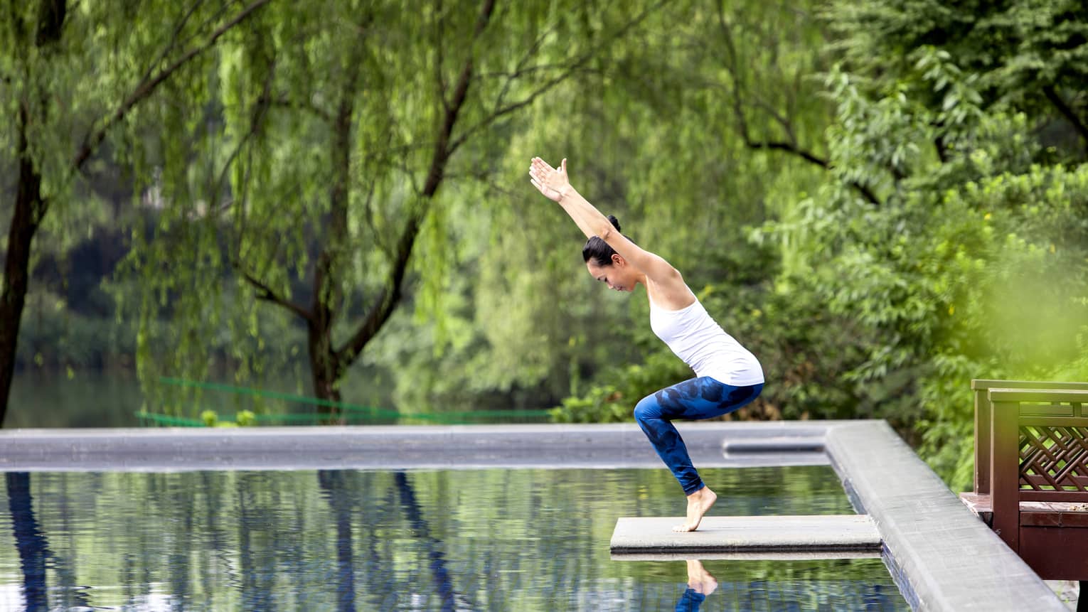 Women stretched in yoga pose on small platform over pond