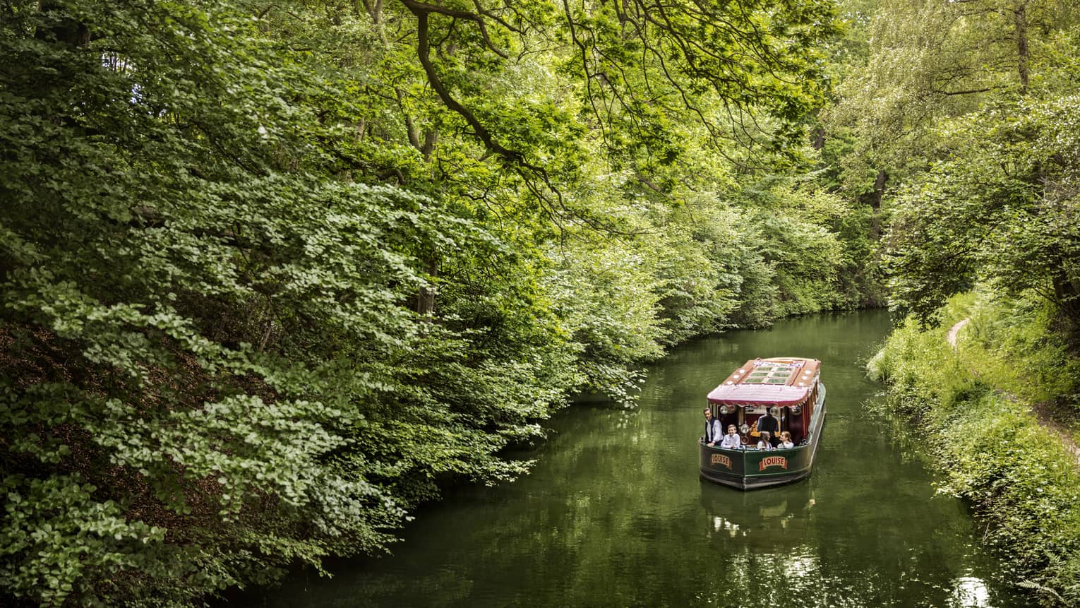 Family on canal boat Louise rides along forest-lined river 