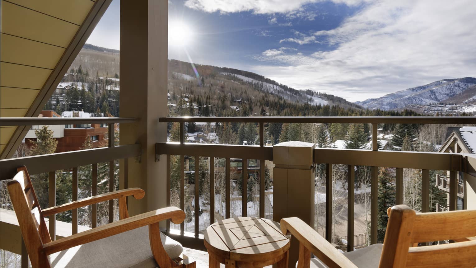 Mountain-view balcony with two wooden chairs and a small wooden, round table