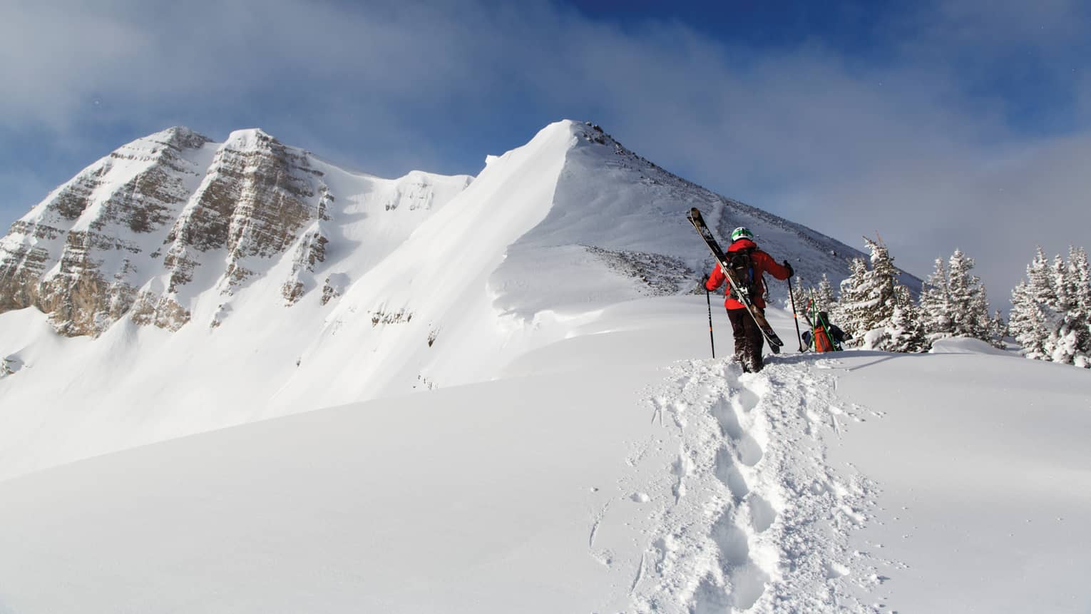 Two people with skis on their backs walking in snow.