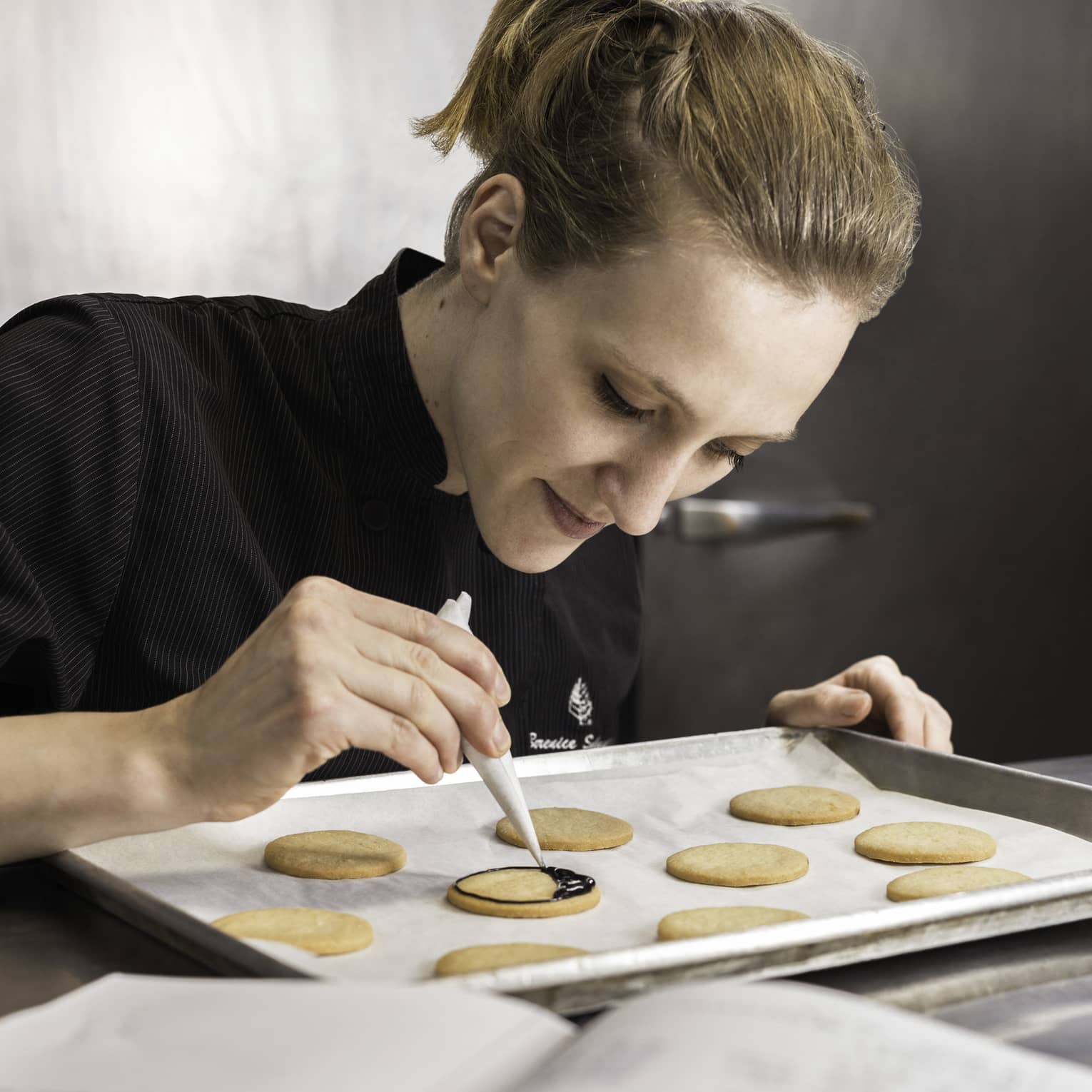 Pastry Chef adding chocolate garnish to row of cookies on baking pan