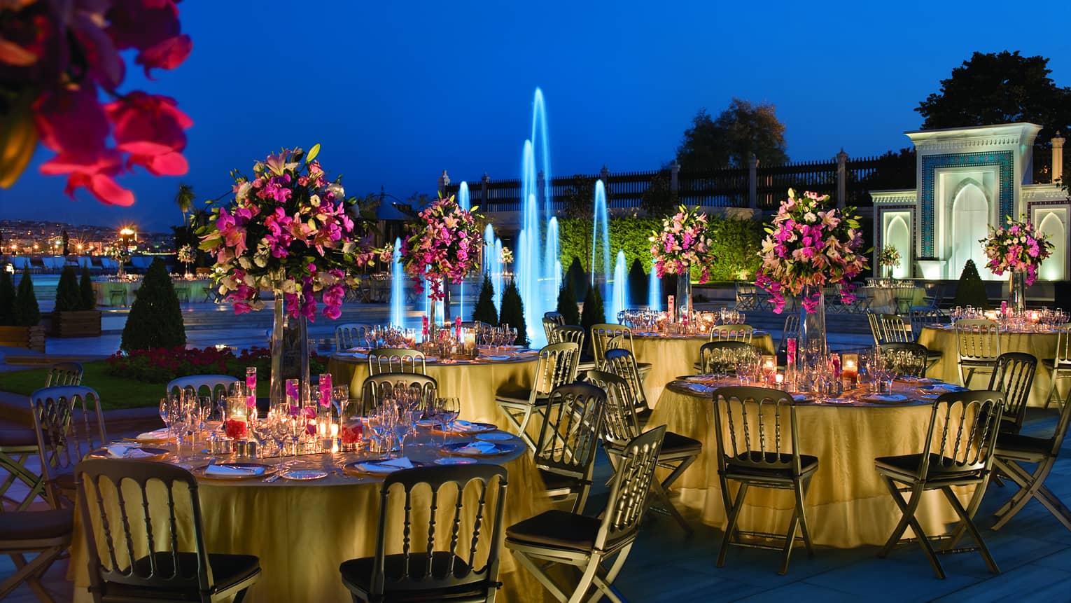 Wedding reception banquet tables with flowers at night in front of fountain with blue lights