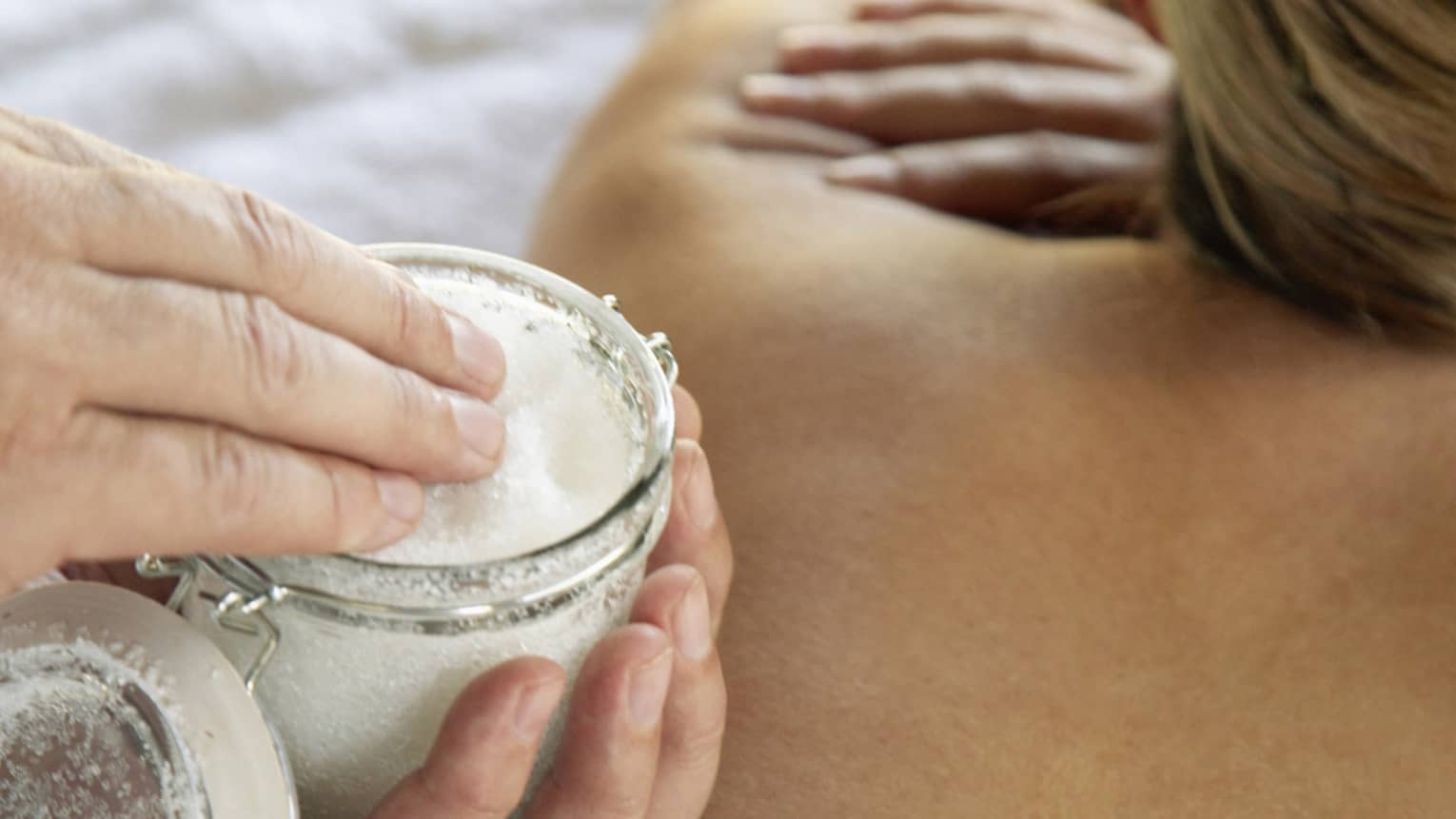 Jar of sea salt scrub above woman's bare back in spa