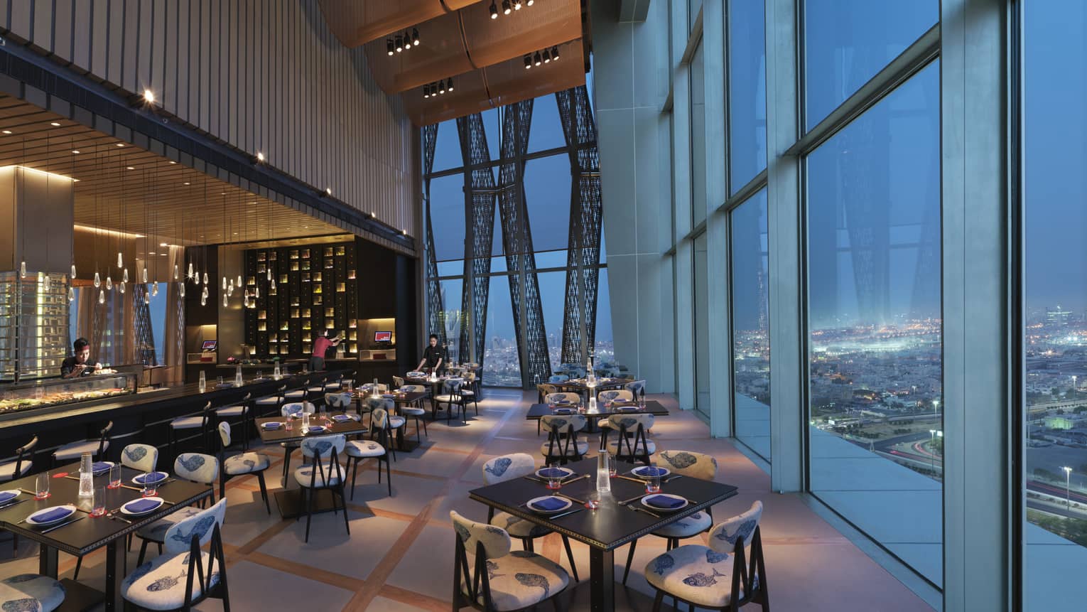 Dimly-lit Sintoho Restaurant at dusk, bar and dining tables and chairs under soaring ceilings, beside glass windows on wall