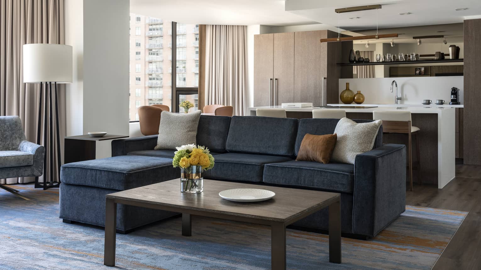Living room with dark grey sofa, wooden coffee table, kitchen in the back