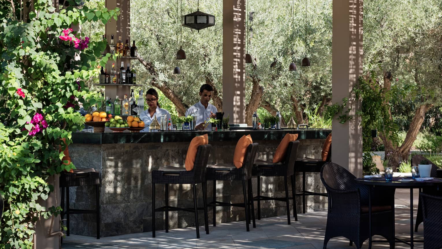Bartenders mix cocktails at small outdoor bar on garden patio