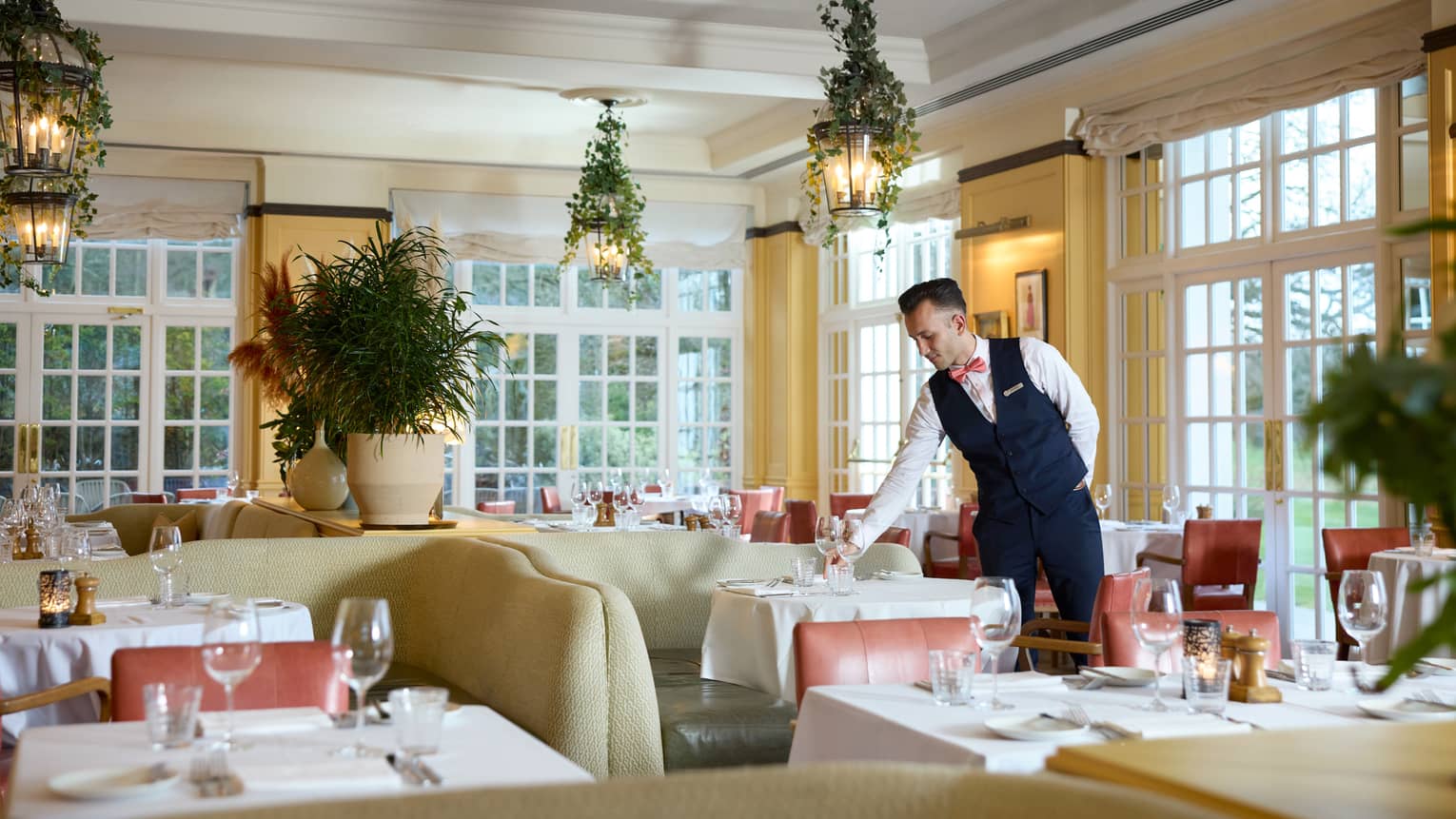 Server sets wine glass on table in elegant, bright restaurant dining room