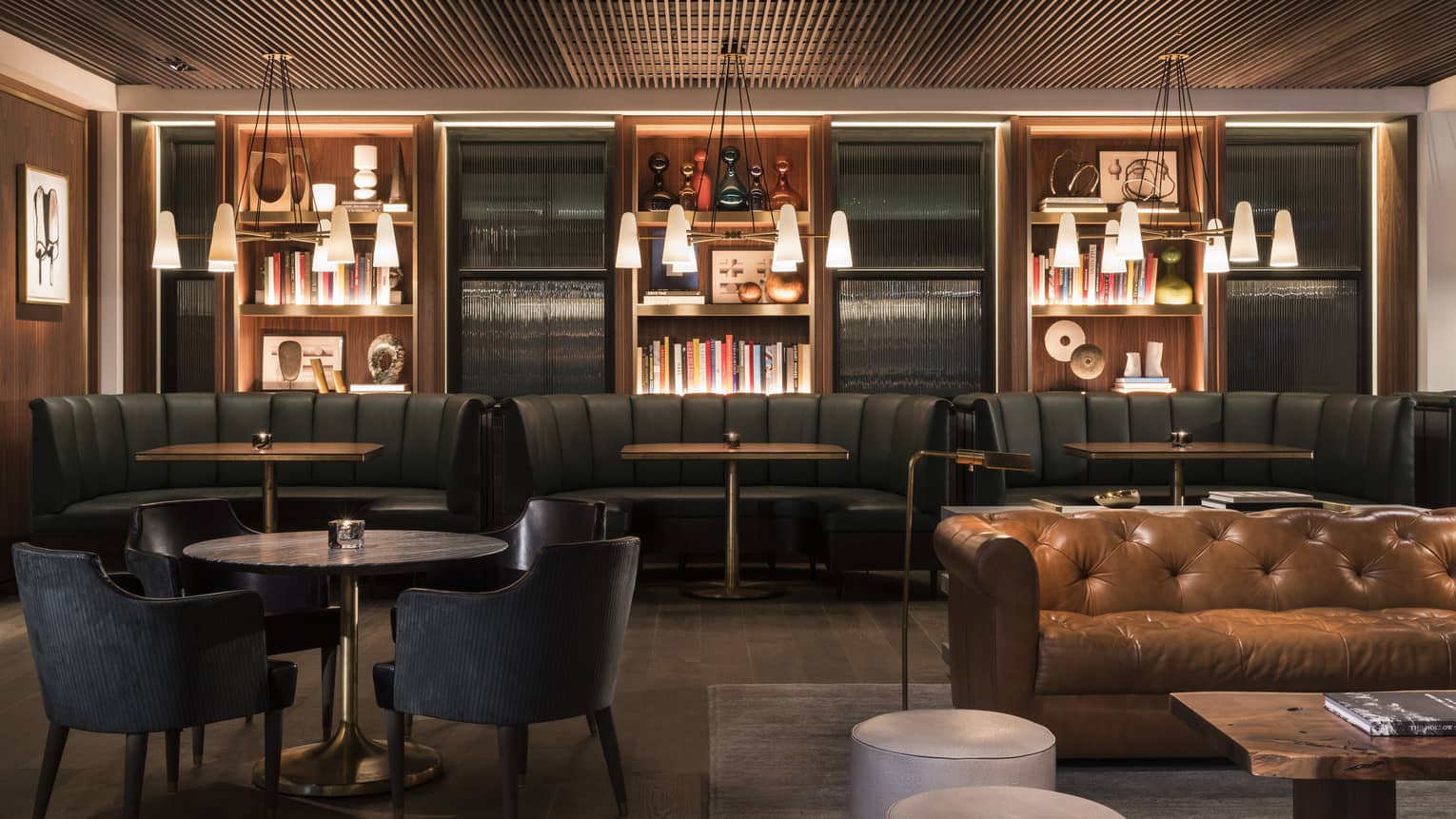 A dining area with black round booths, a brown sofa, a small black table with chairs, and hanging lights.