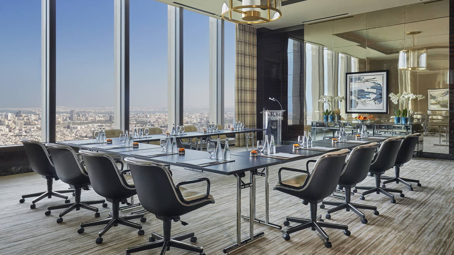 Meeting room with glass modular table lined with swivel chairs, floor-to-ceiling glass windows