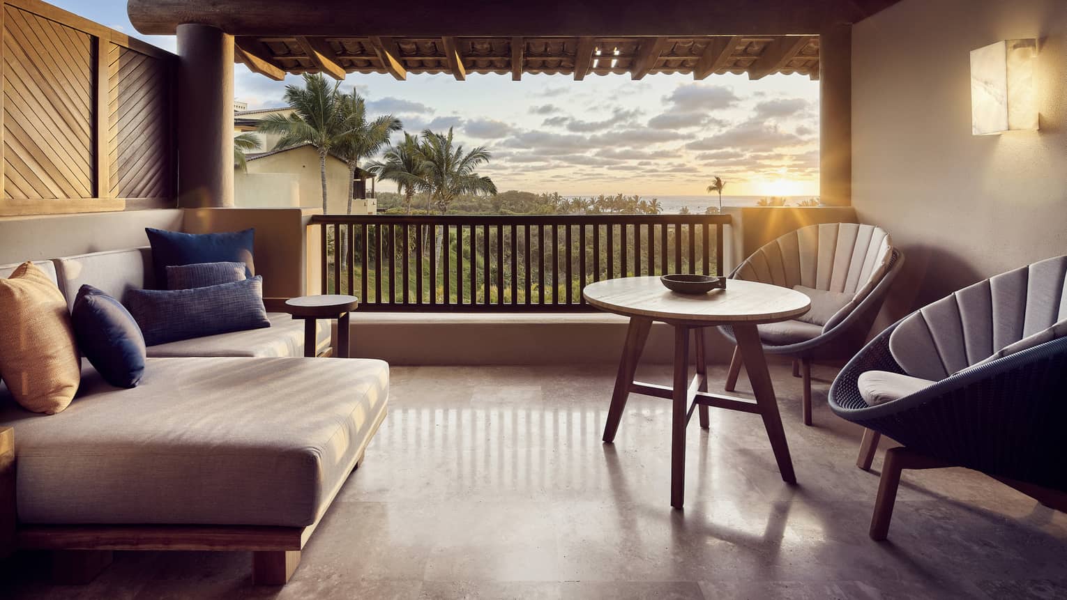 A sunlit hotel balcony with two chairs, a small table, and a sofa.