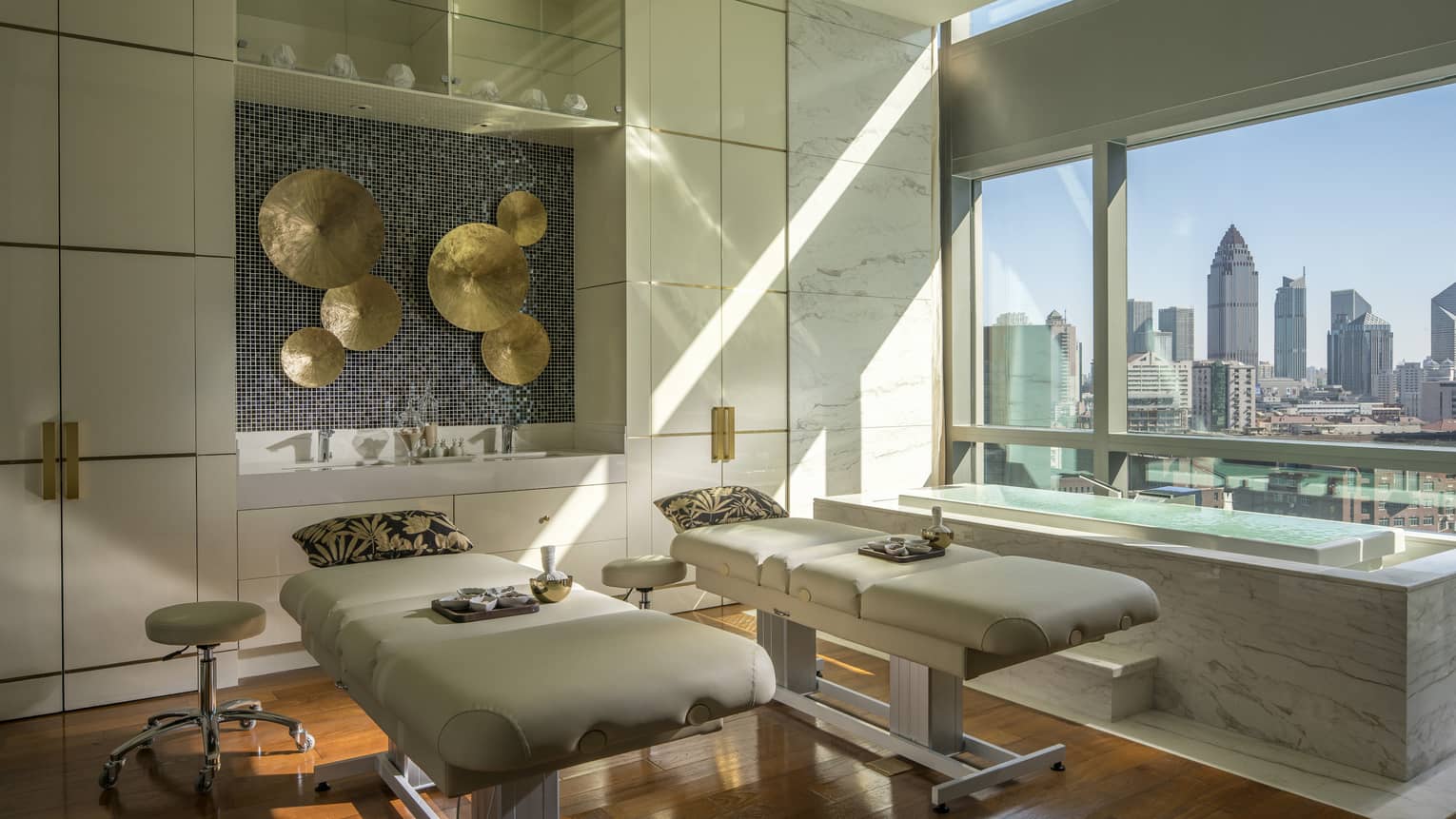 Couples massage beds with pillows under brass disc art on walls in L’Océan Spa