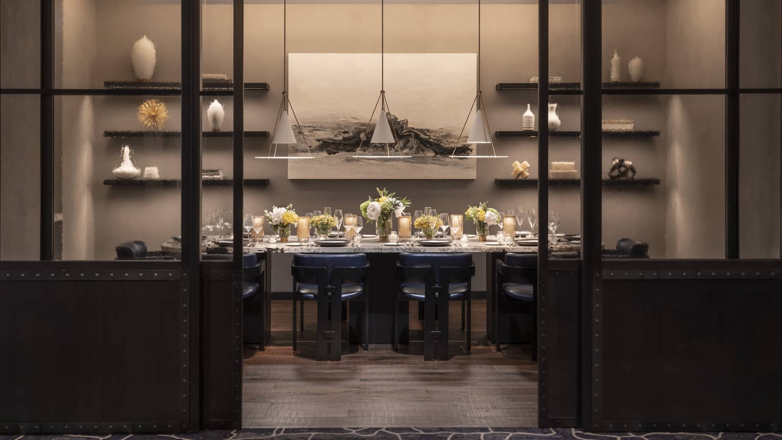 A private dining room with a large table covered in flowers and a painting and shelves on a wall.