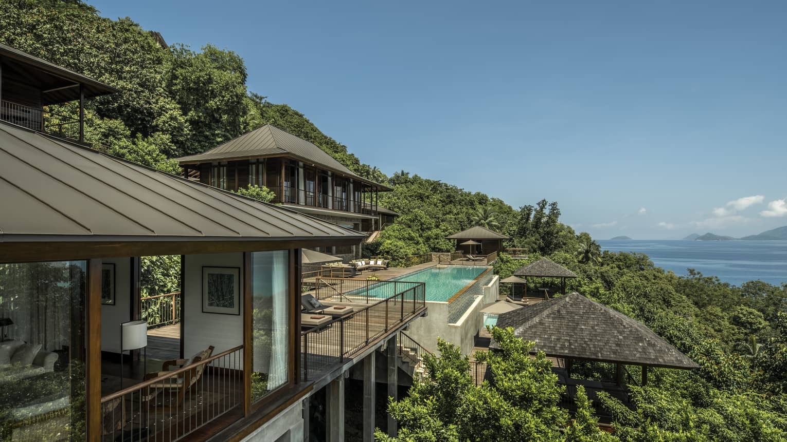 Four-Bedroom Residence Villa roofs, patios amid trees on mountain, ocean below