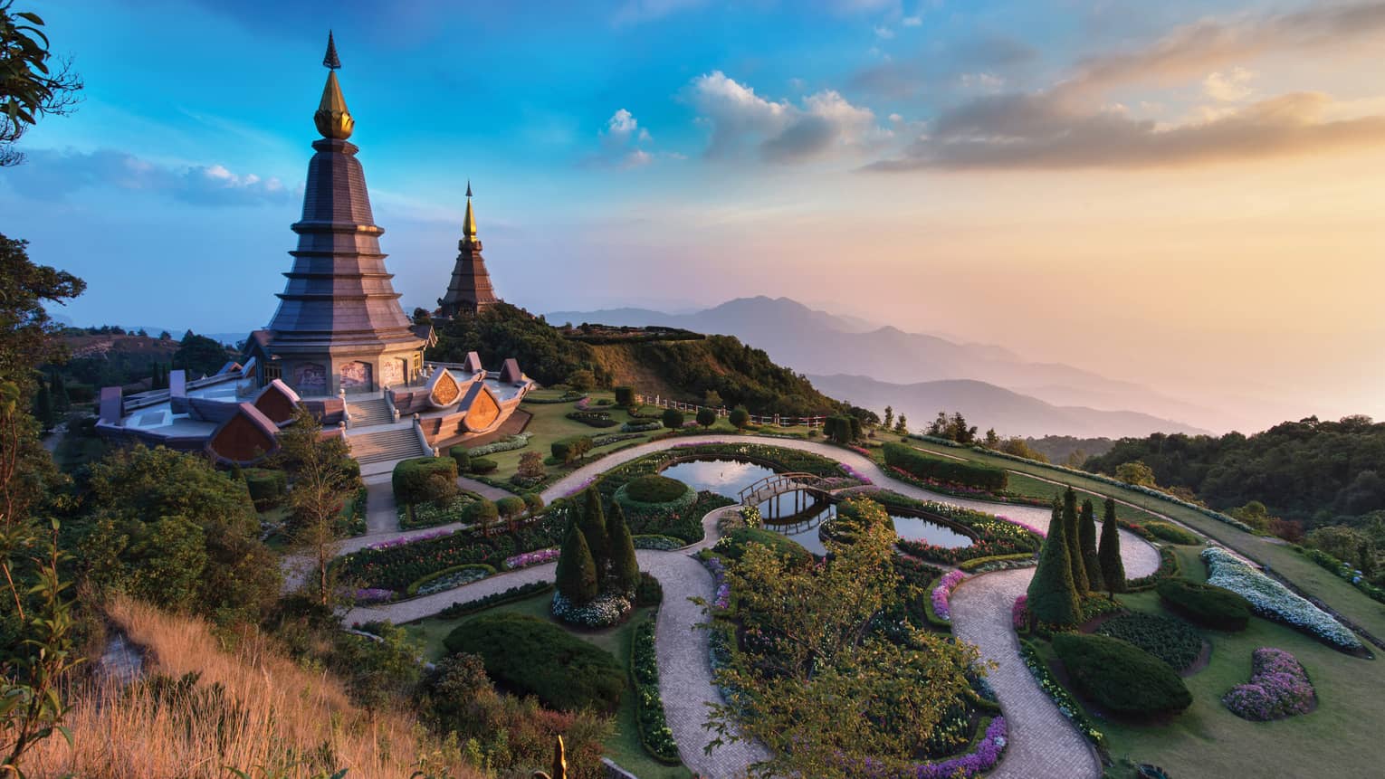 Majestic twin pagodas surrounded by lush gardens and winding paths, set against a backdrop of misty mountains at sunset.