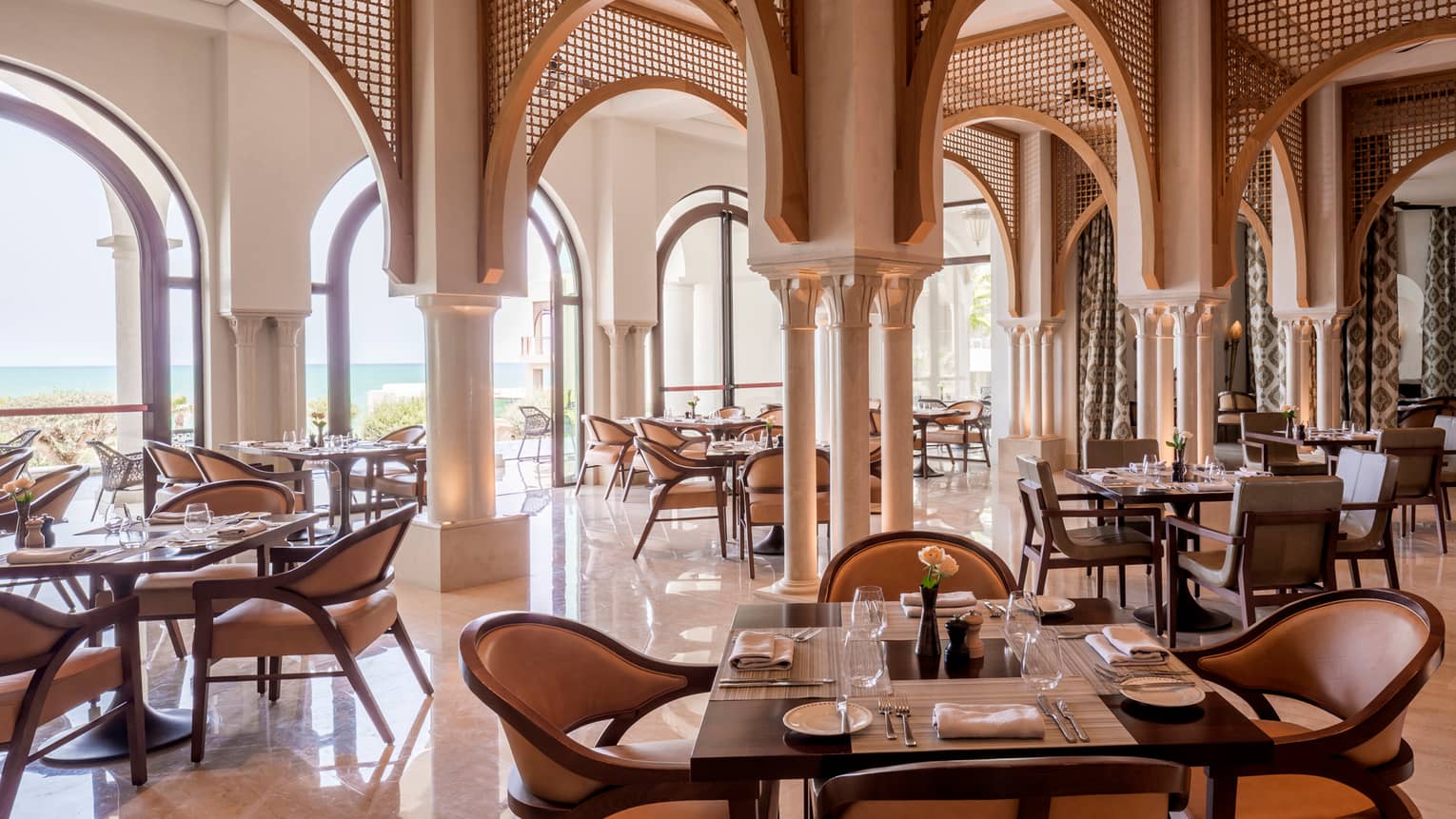 Restaurant dining area with archways, set square tables, tan leather dining chairs, water view
