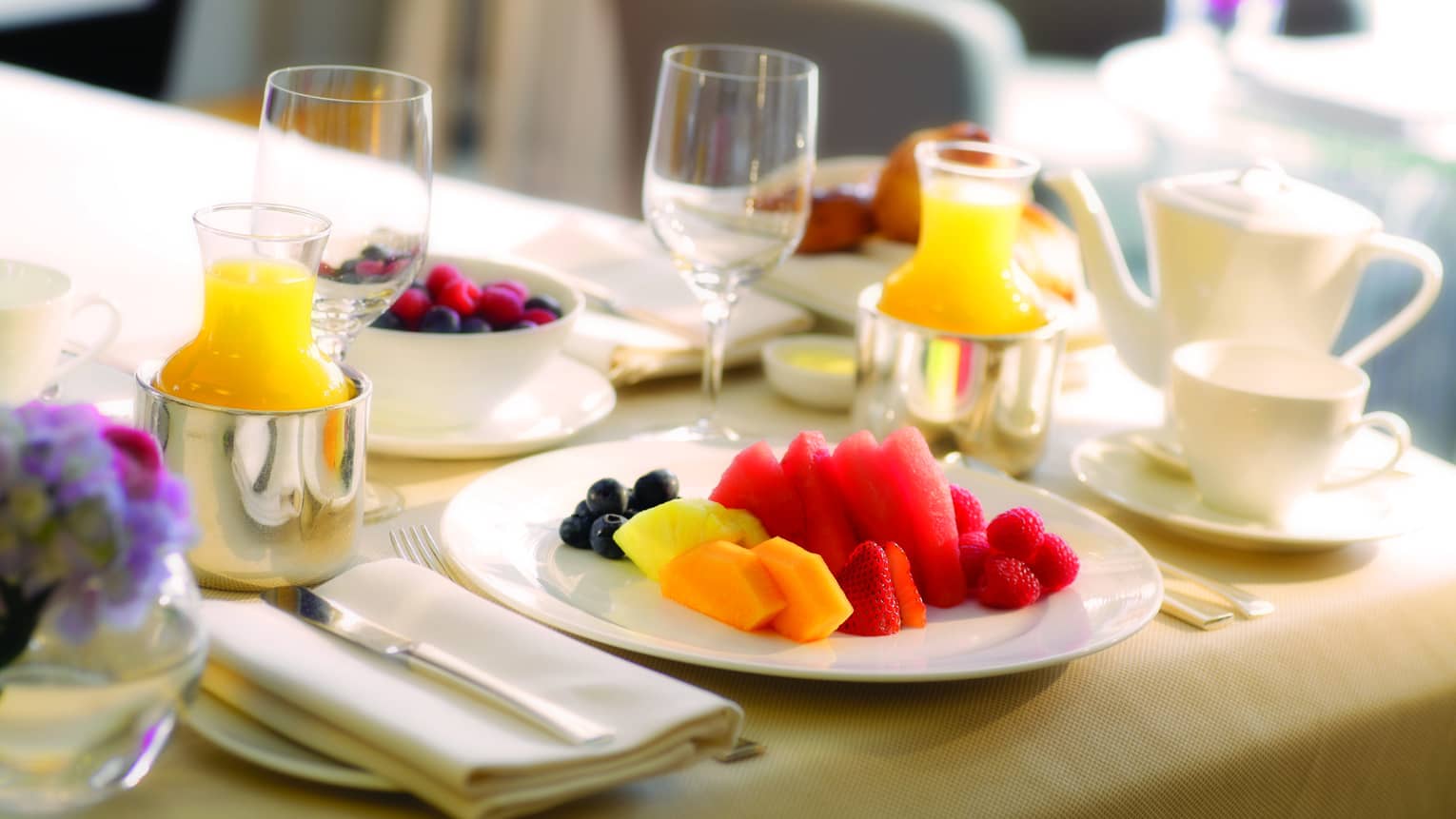 Close-up of in-room dining table service with plate of fresh melon and berries, tea and orange juice