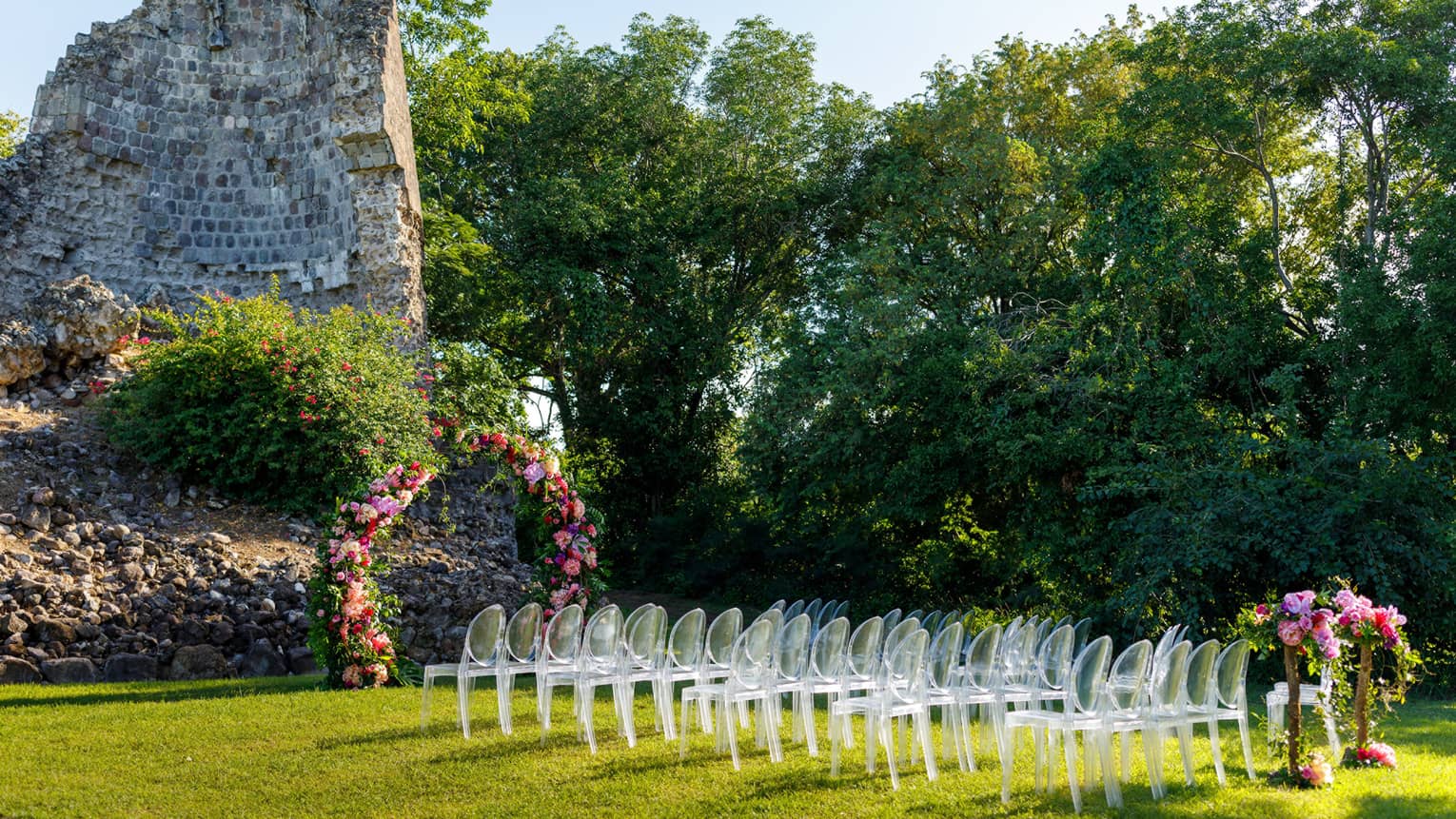 Outdoor wedding setup at Tea Mill rock structure, lucite chair grouping, flowers, flanked by bushes