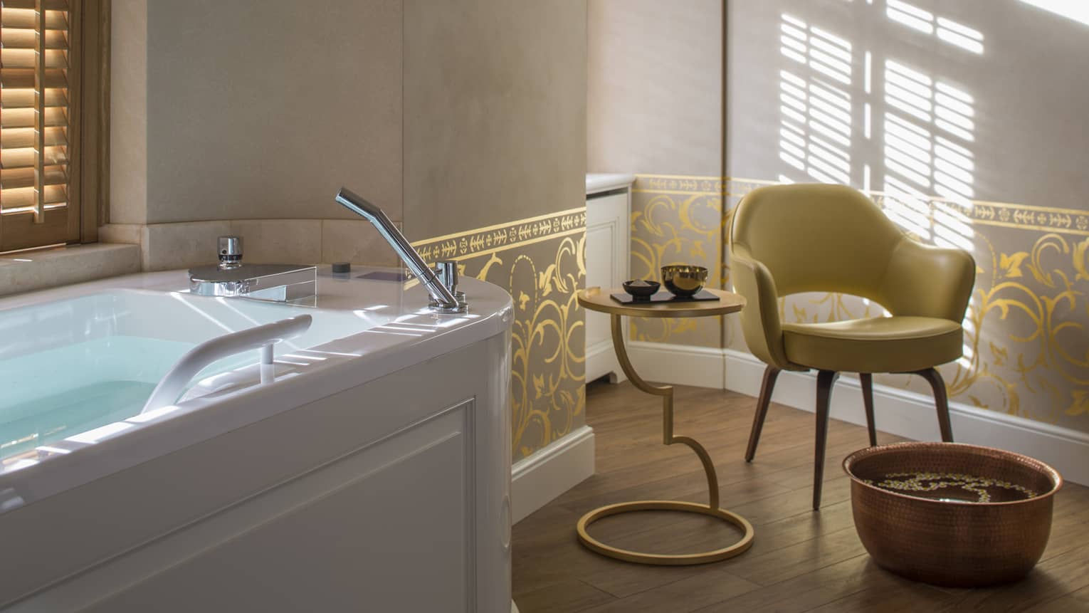 Mid-century style yellow armchair next to round foot bath, side table with gold bowls, gold-and-grey pattern wallpaper