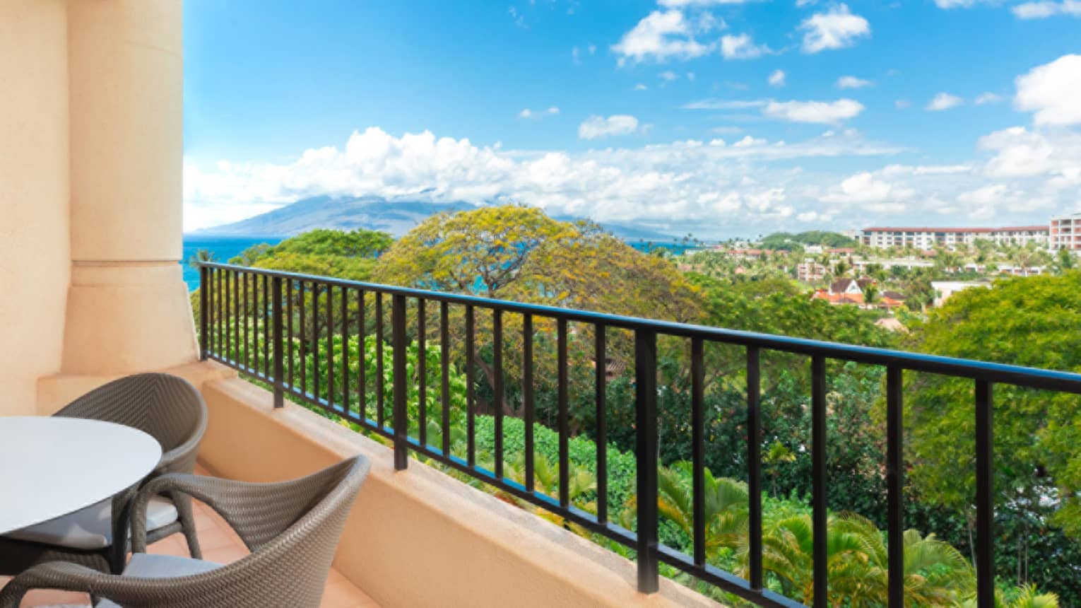 Balcony view overlooking lush greenery, distant buildings and mountain under a bright blue sky with clouds
