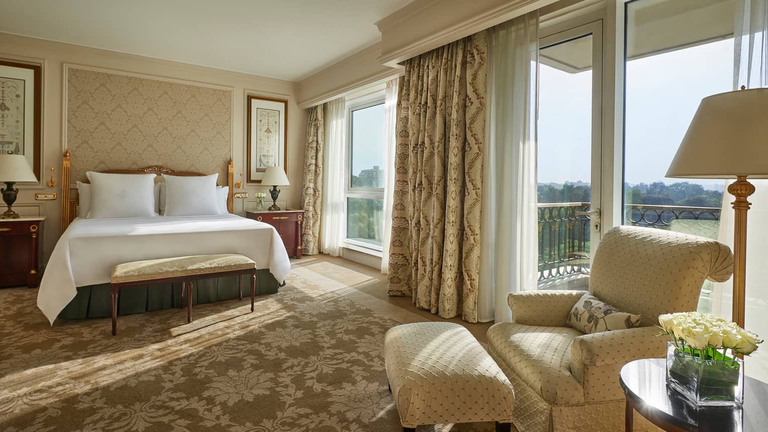 Deluxe Room bed, cream-coloured armchair beside sunny floor-to-ceiling patio door and window