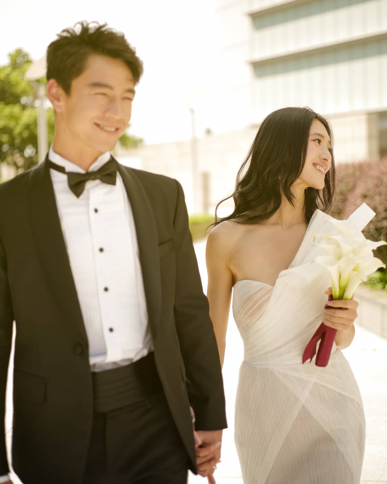 Bride and groom walk hand in hand outside in urban setting