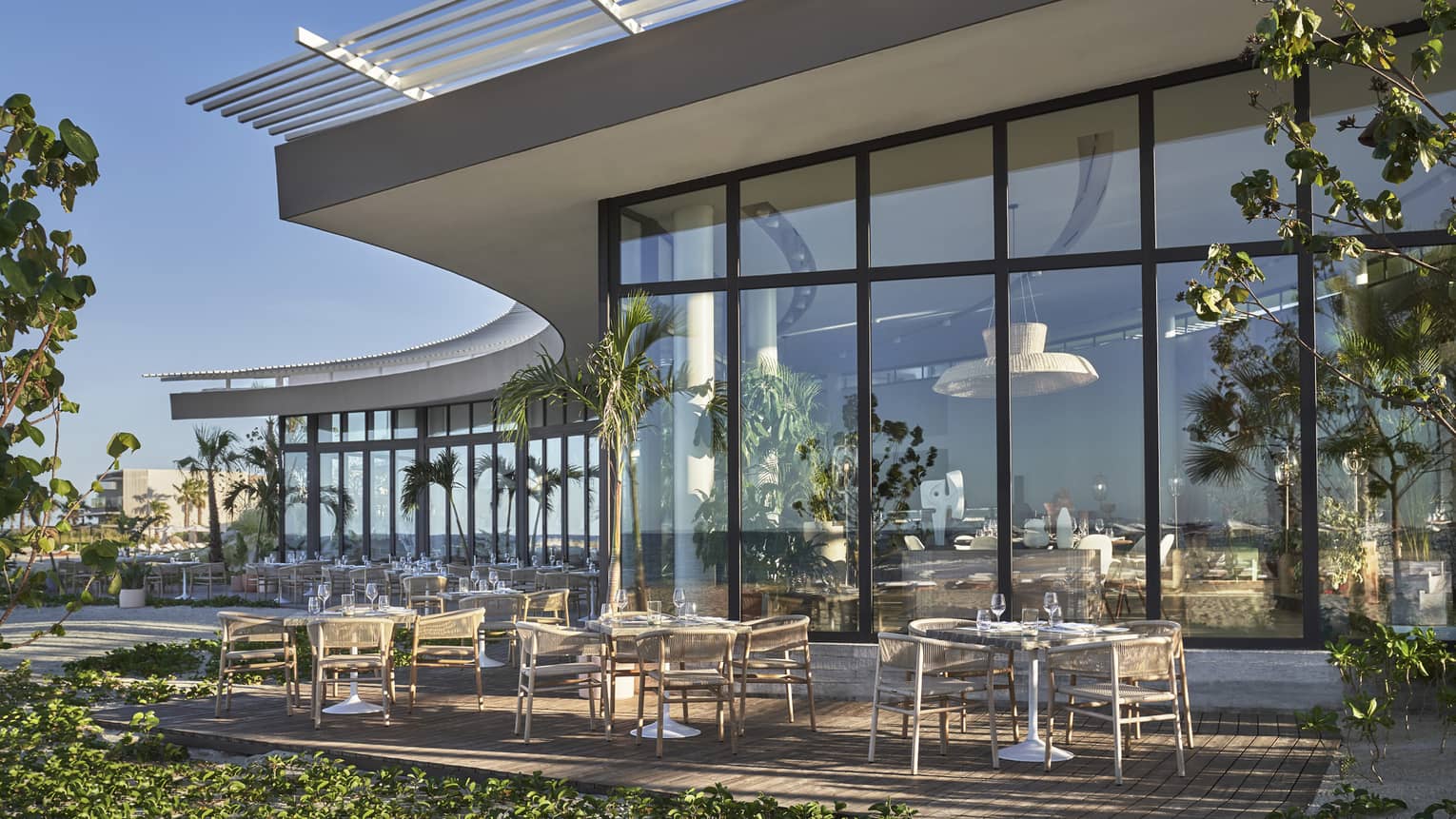 A large dining outlet with floor to ceiling windows with tables and plants outside.