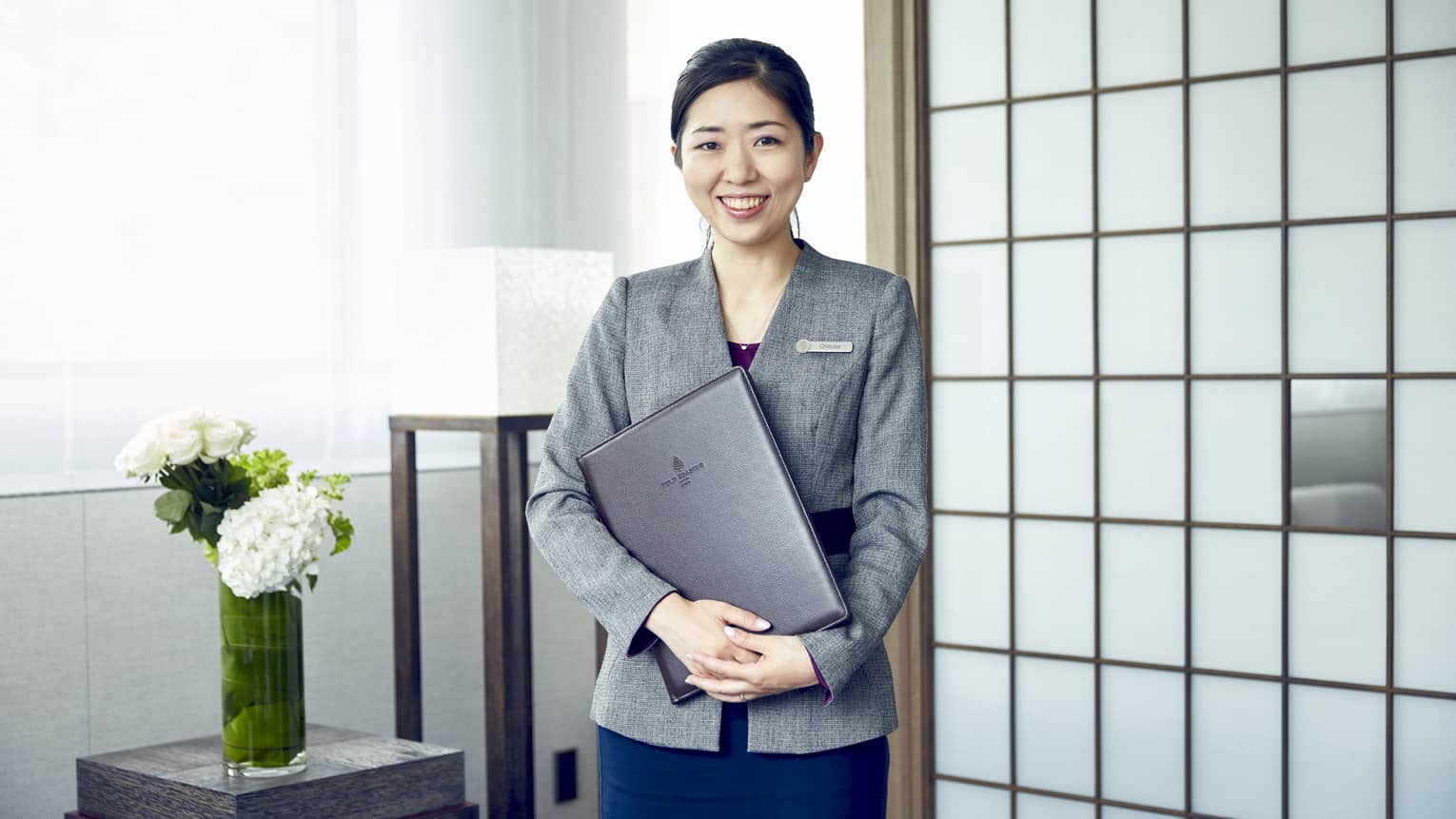 Portrait photo of smiling wedding consultant holding binder against wall