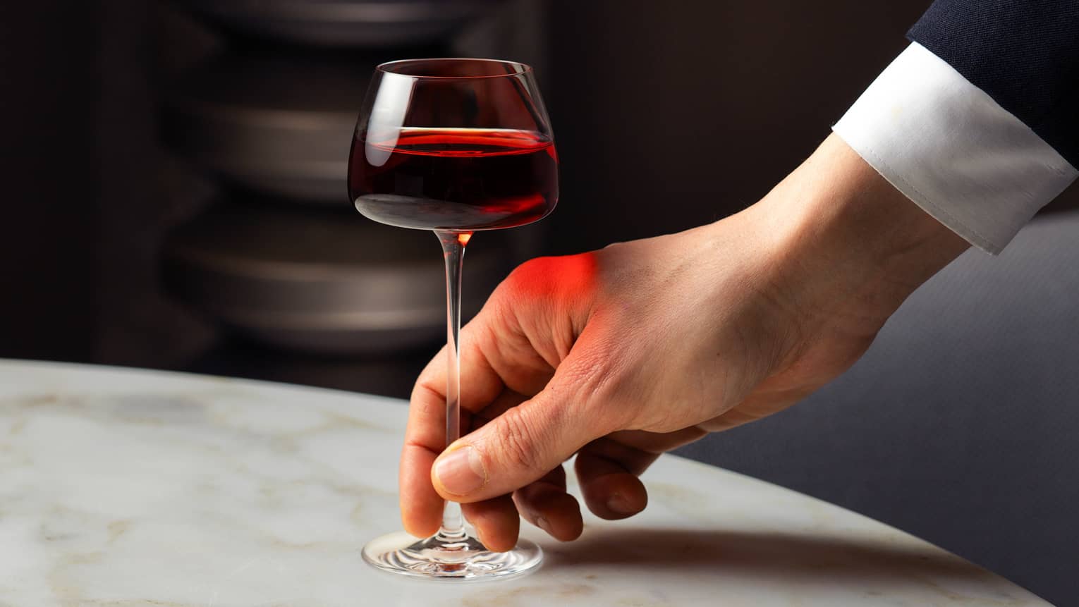 A hand sits down a glass of red wine on a white marble tabletop