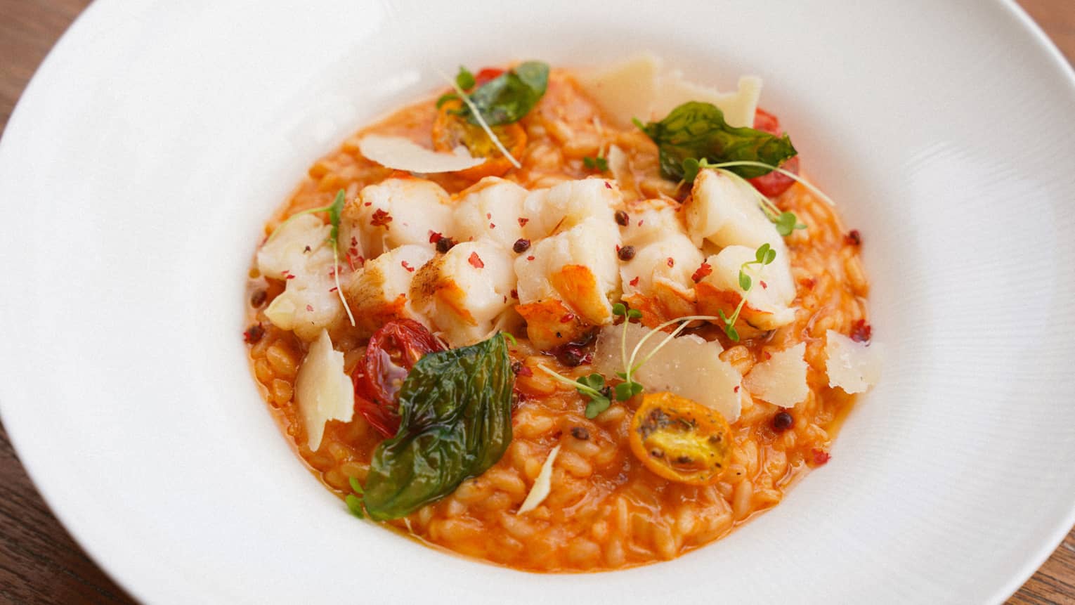 A white plate holds rice in a reddish-orange sauce topped by pieces of lobster and various garnishes.