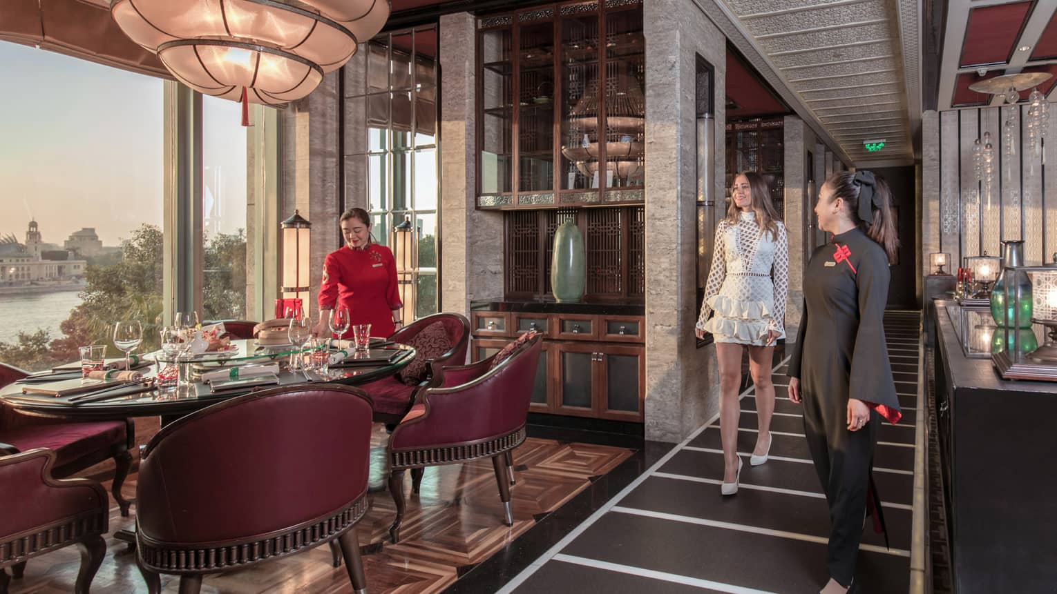 A guest is shown to her table, surrounded by burgundy chairs, in a luxurious restaurant with opulent decorations.