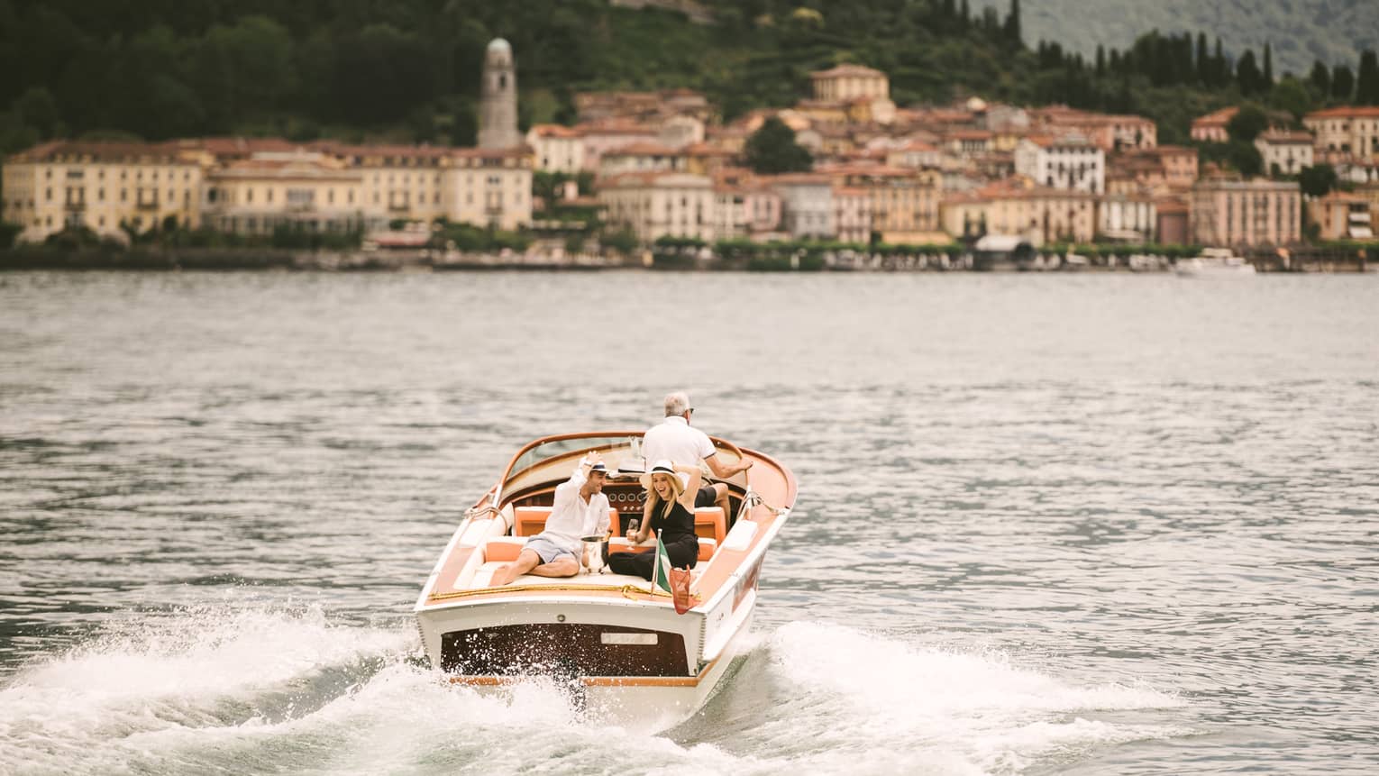 Couple laugh, drink Champagne on back of powerboat on Lake Como
