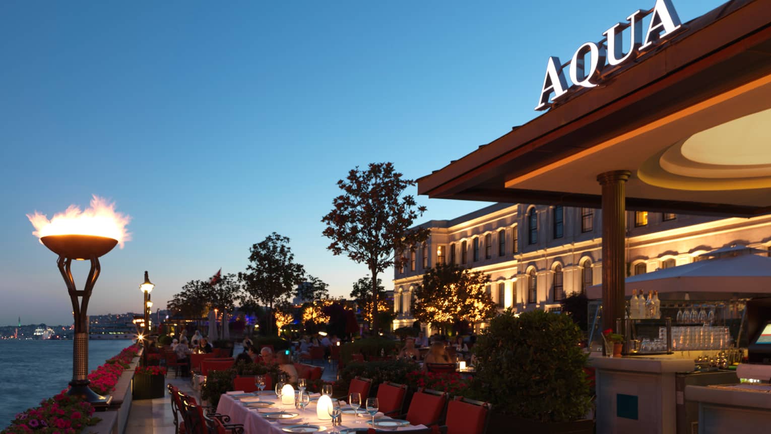Tall torches over Aqua dining tables, Aqua sign on building at dusk