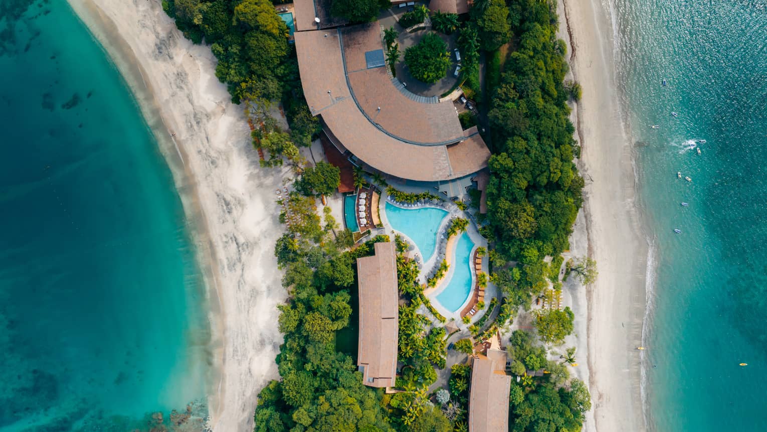 Aerial view of pool and buildings on a strip of green land bookended by water on either side