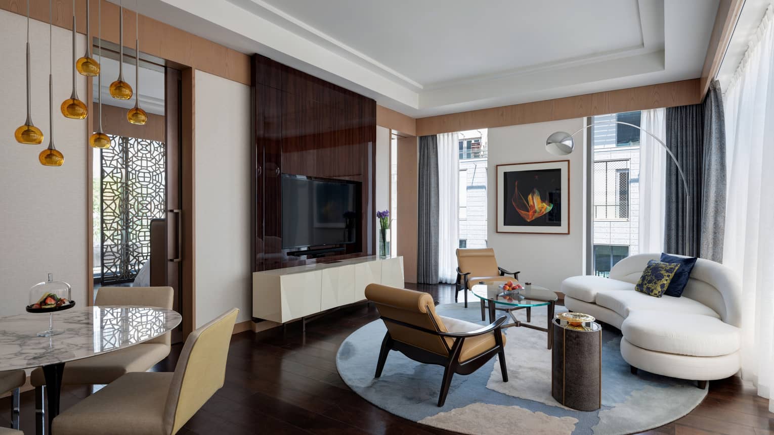 Living room with large TV, white curved sofa, two leather arm chairs, dining table