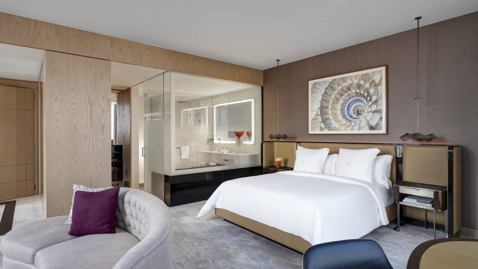 Bedroom with king bed, artwork on wall, curved sofa, open bathroom