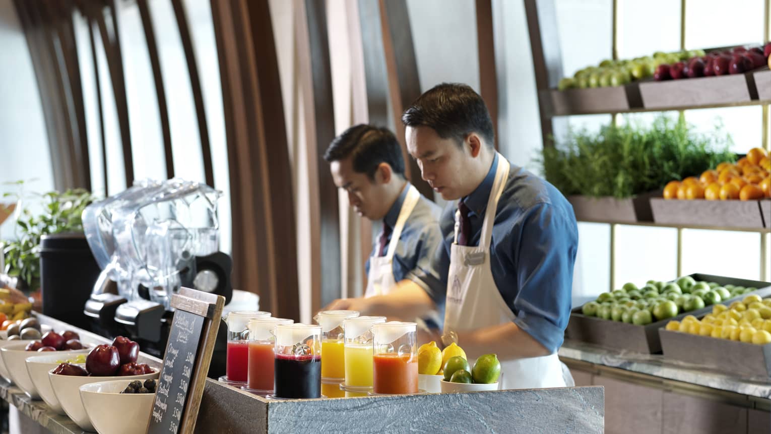 Two baristas standing at a counter in front of a tray of vegetables.