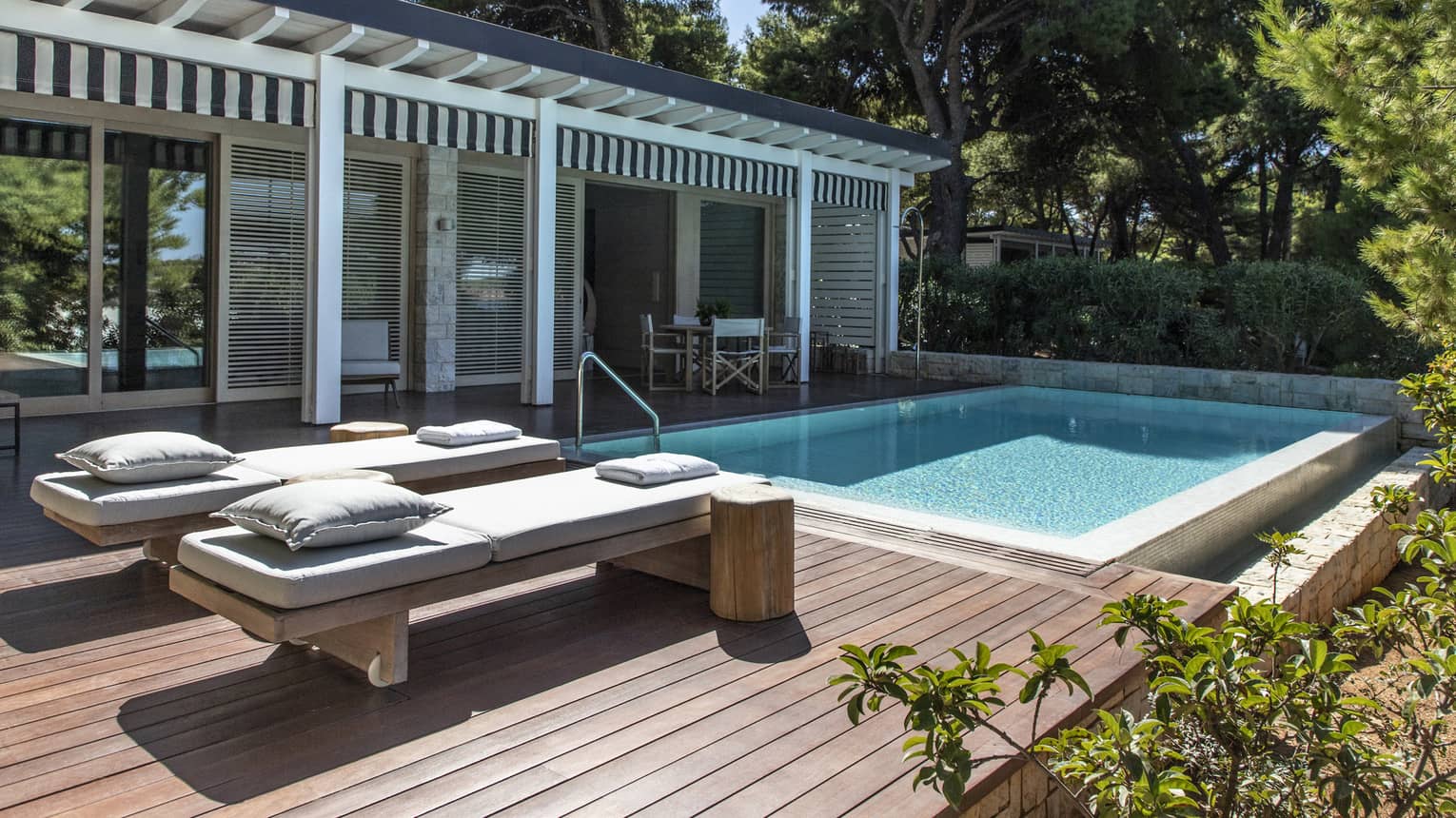 Private wooden deck with two lounge chairs and pool, surrounded by greenery