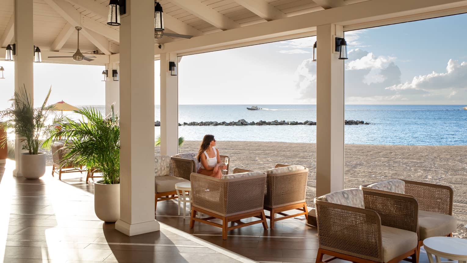 A woman sitting at a dining outlet that is open to a beach.