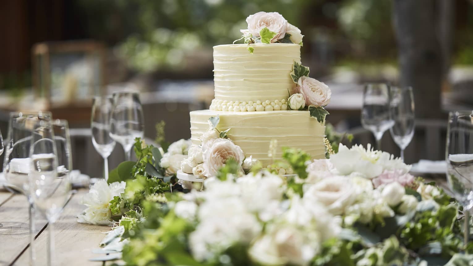 Two-tiered white wedding cake on banquet table with wine glasses, flowers