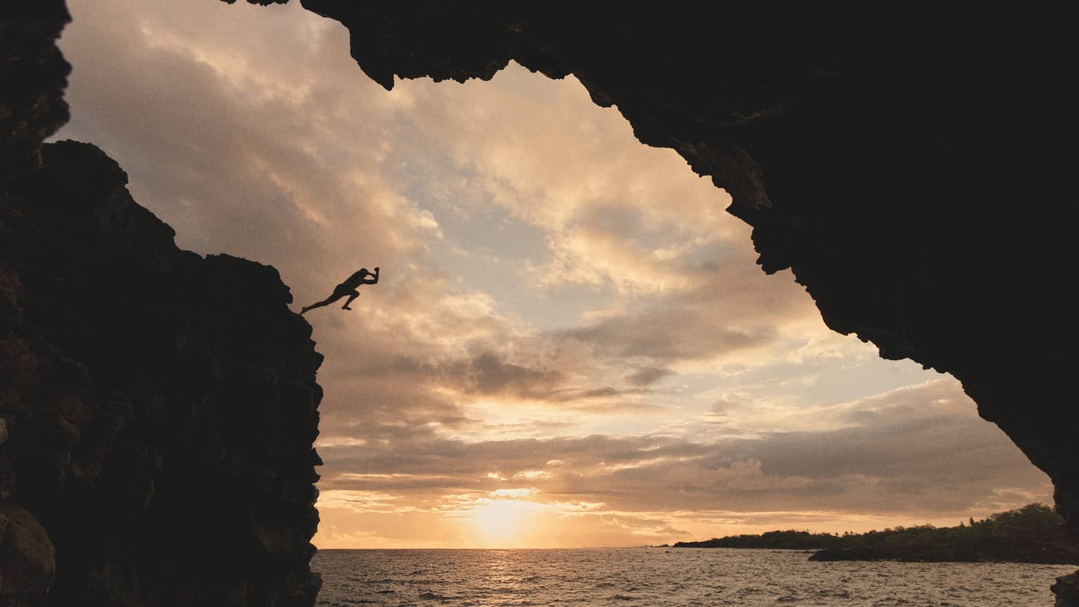 Person jumps off cliff into ocean at sunset in tropical destination