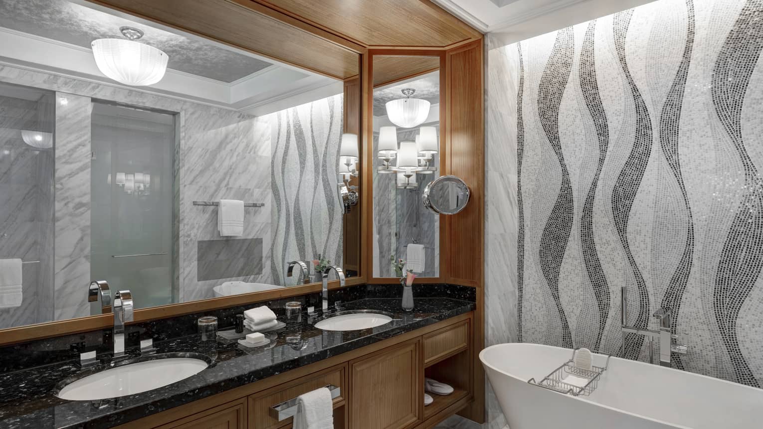 Bathroom with grey mosaic tiled wall, freestanding tub, wooden vanity with black top