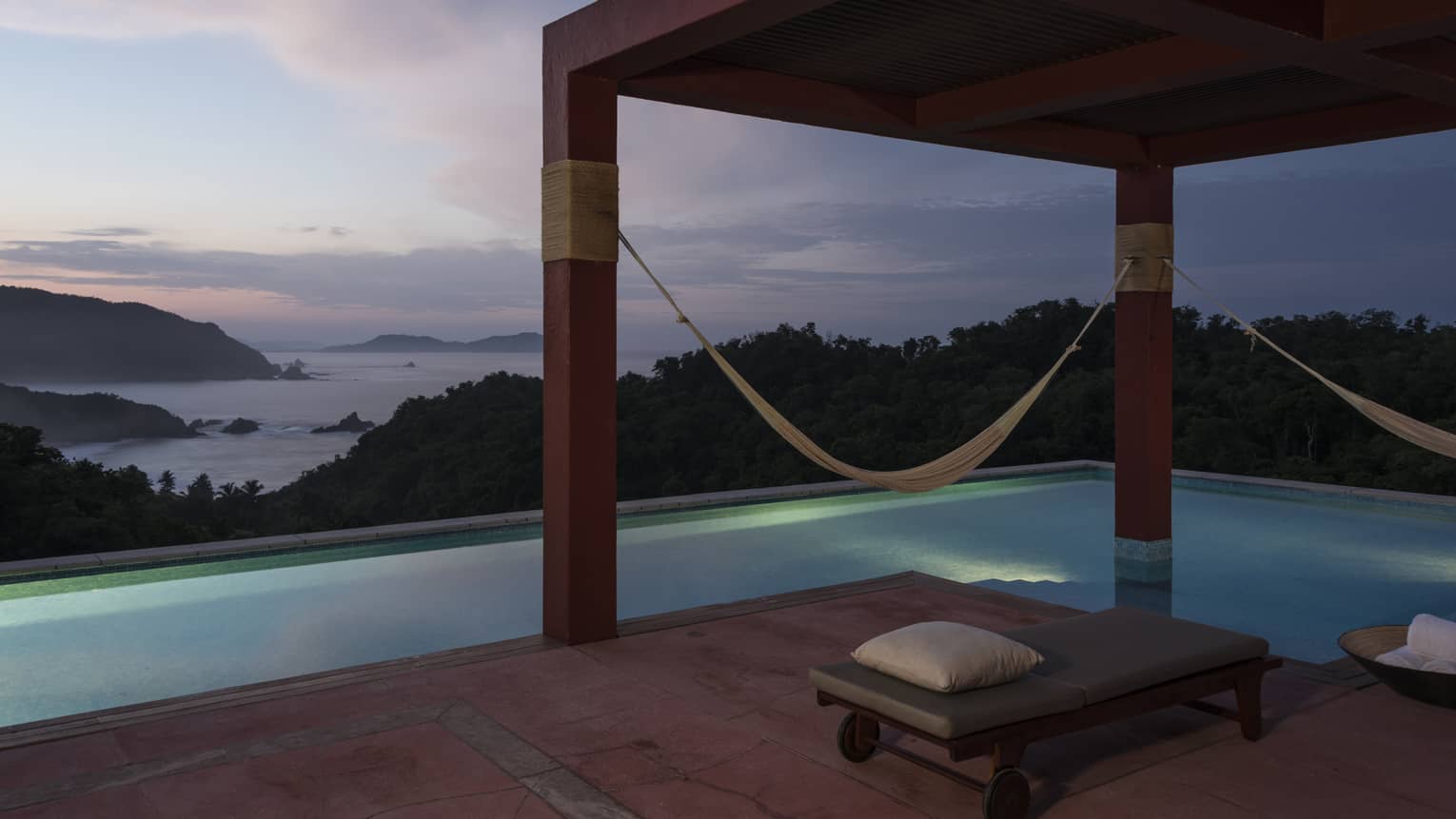 Pool and pergola with hammocks overlooking beach at dusk