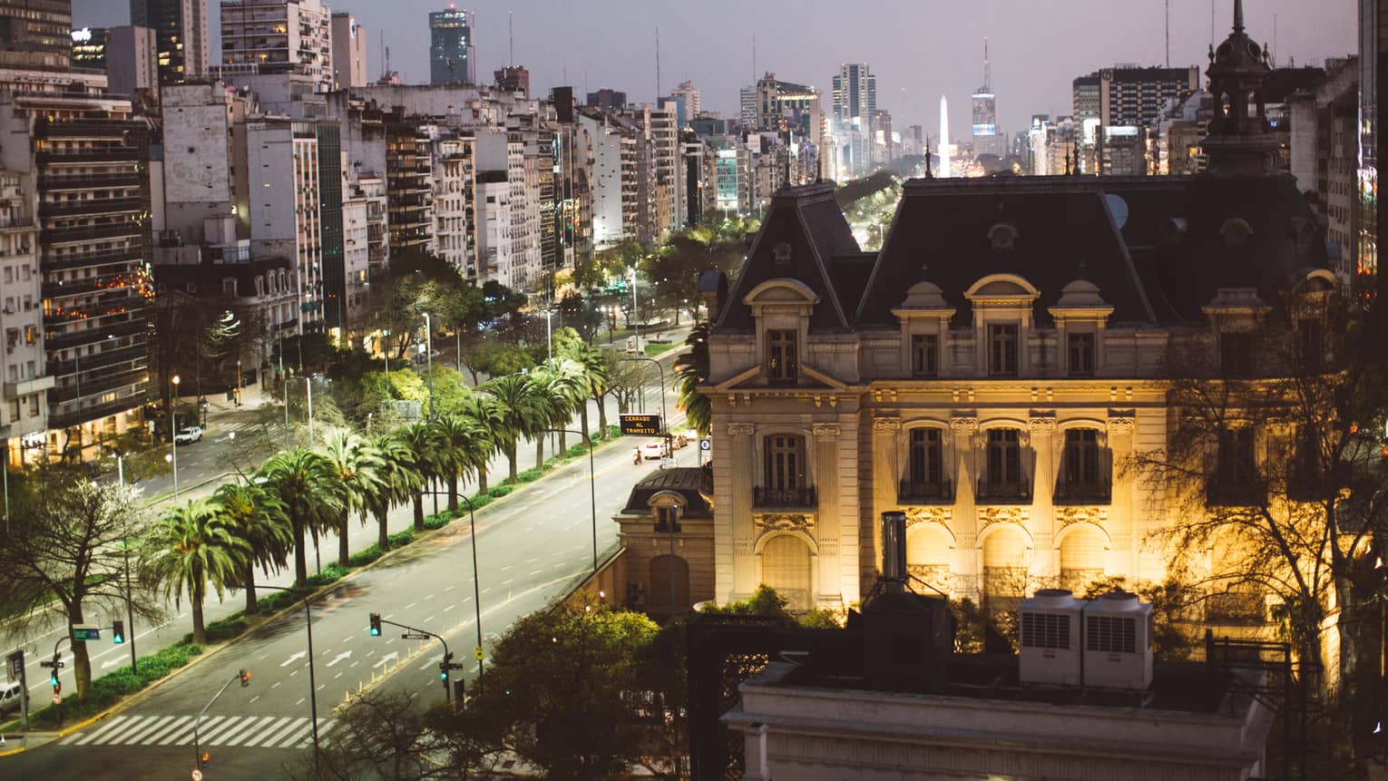 Exterior of Four Seasons Hotel Buenos Aires lit up at night next to a tree-line avenue and various city buildings across the street